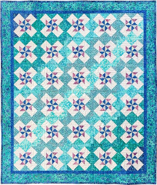 A square quilt with a repeating pinwheel pattern, featuring white diamond sections with pink and blue starburst centers, surrounded by teal and turquoise checkered fields and a blue border.